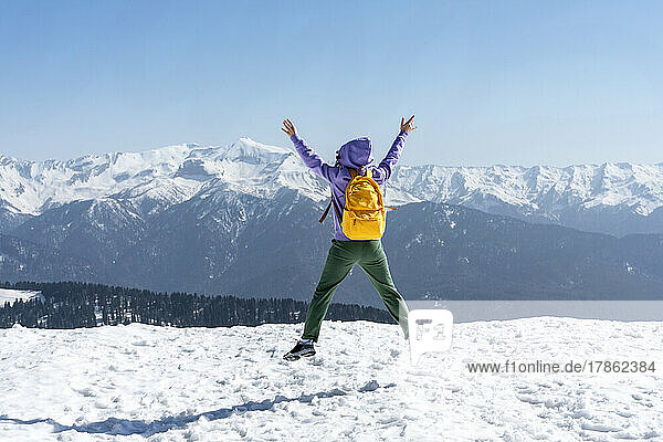 Young happy woman with yellow backpack jumping in snowy mountains