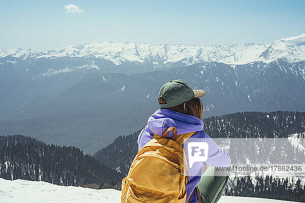 Young woman with yellow backpack sitting in snowy mountains