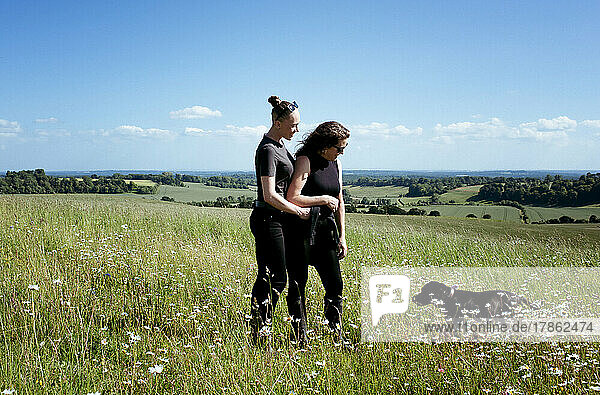 lesbian couple hugging whilst walking their dog in the countryside