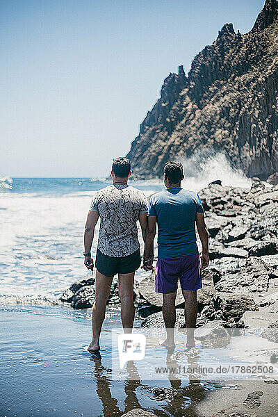 man with his boyfriend holding hands on beach on sunny day