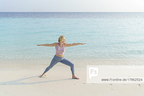 A woman on the beach does sports  yoga.