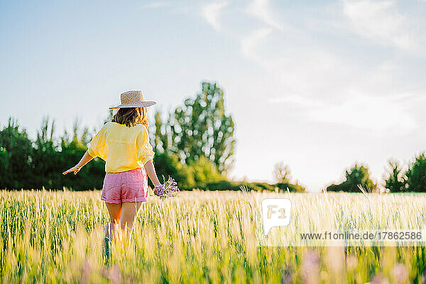 Pretty countryside woman in straw hat walking in wheat field.