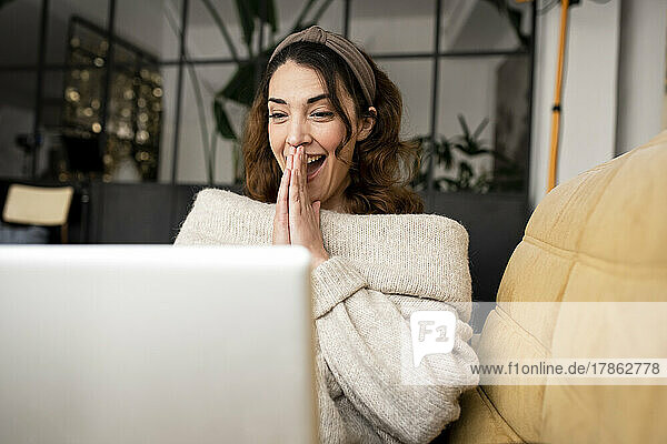 Excited woman looking at laptop screen sitting on cozy sofa at home