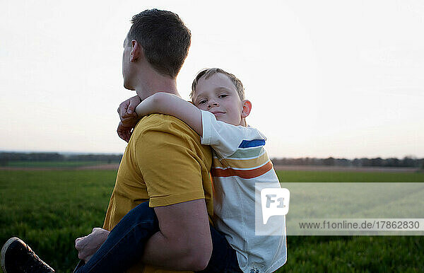 father giving son piggy back ride wjilst walking at sunset