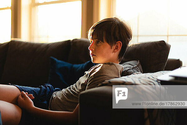 Boy sitting and relaxing on couch in warm window light at home.