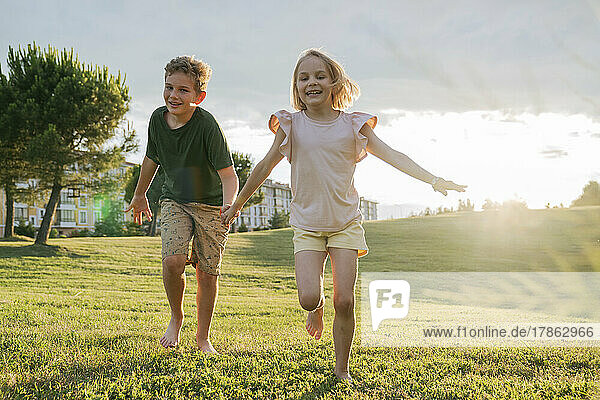 Brother and sister running on the grass at sunset.