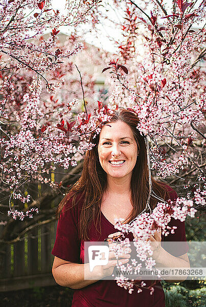 Happy woman standing among branches of flowering tree in spring.