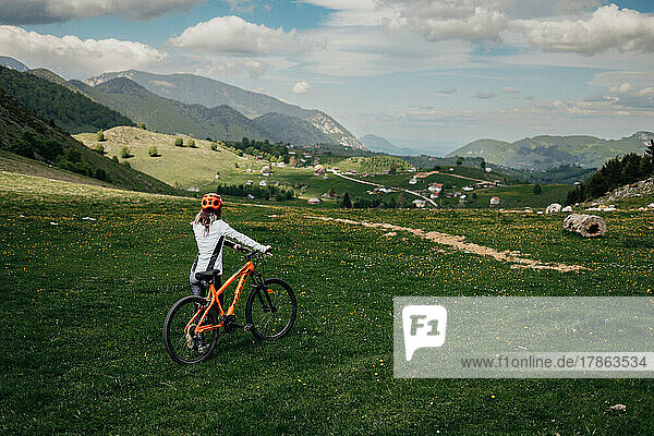 Cyclist with helmet holds her bicycle and looks at the valley