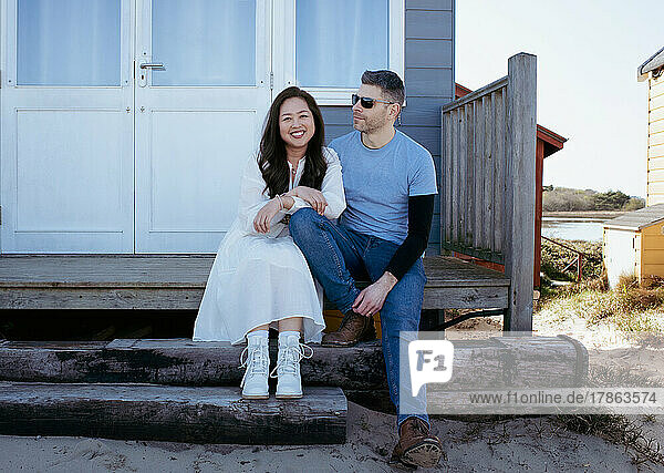 beautiful mixed race couple sat on the beach at a beach hut in summer