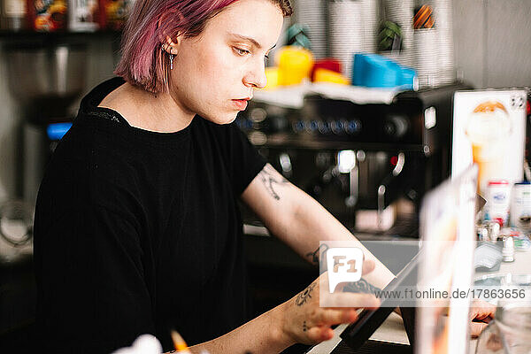 Young female barista working at checkout counter in coffee shop