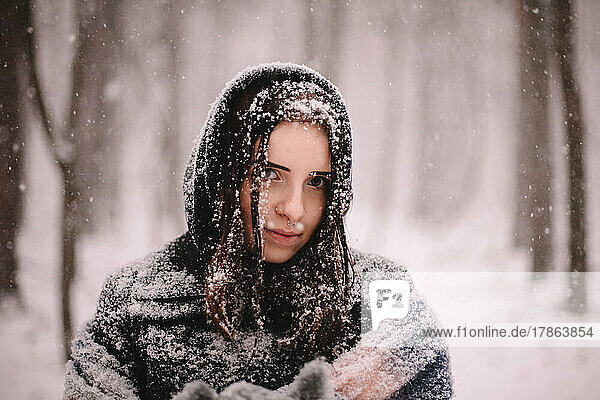 Portrait of young woman covered with snow standing in park in winter
