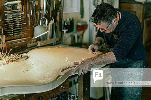 luthier working on a handmade double bass front table in his workshop