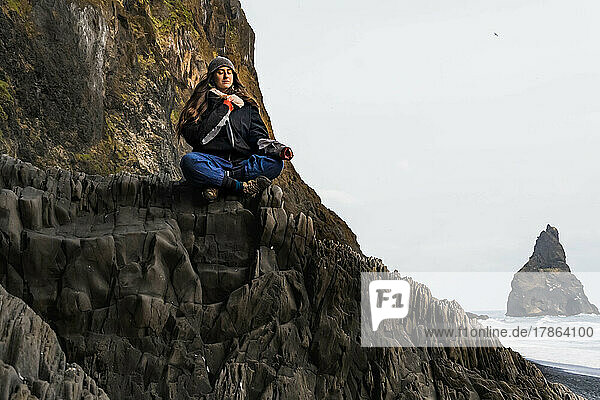 woman meditating on top of some rocks on a black beach