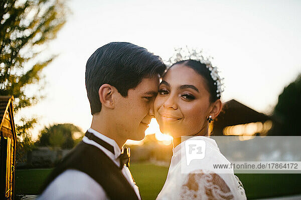 Bride and groom of mixed race snuggle in the sunset and golden light
