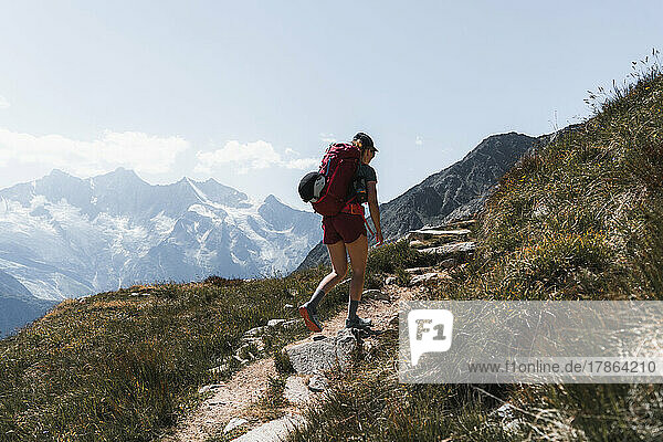 Female hiker carrying backpack walking uphill in front of mountains