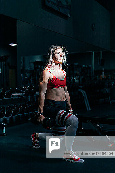 fit woman working out in dark gym with sun on her face
