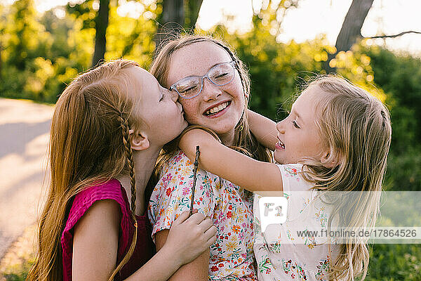 Young sisters laugh  hug and kiss in golden light