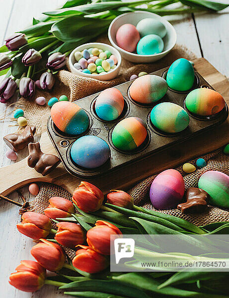 Tray of brightly colored Easter eggs surrounded by tulips.