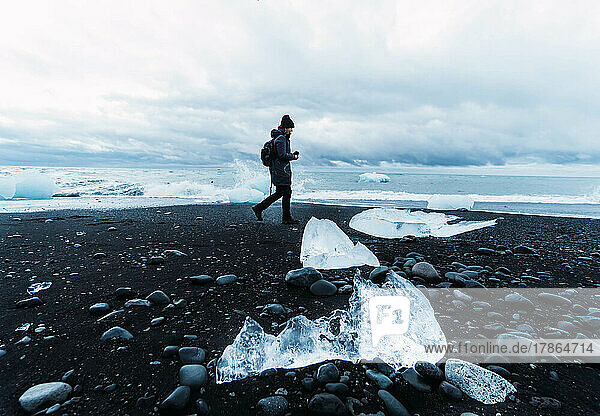 person on black beach surrounded by pieces of ice