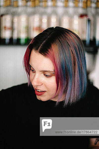 Young female barista with multi colored hair in coffee shop
