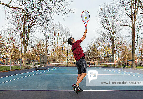 Man playing tennis with teen son on outdoor hard court in spring.