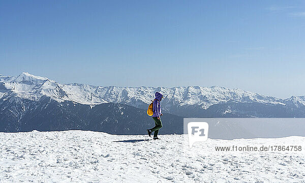 Young woman with yellow backpack walking in snowy mountains