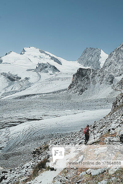 Vertical image of hiker from back walking towards glaciers and peaks