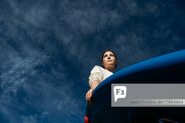 Looking up at teen girl sitting on a sunny day with blue sky
