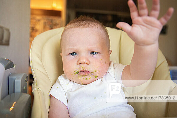 A baby soiled with vegetable puree sits in a children's chair