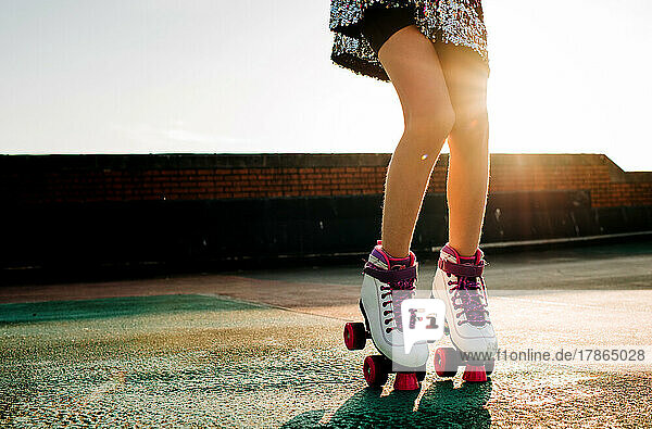Childs legs with roller boots in in a sequin dress dancing at sunset