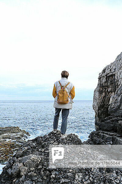 Retired tourist woman standing on black rocks and looking to the sea