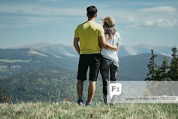 Rear view of young sporty couple hugging and looking at the mountains