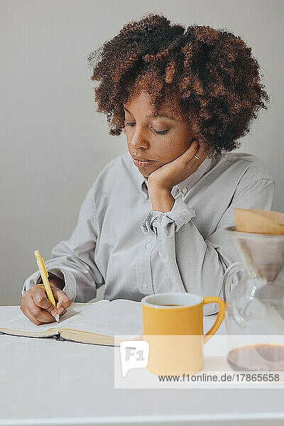 A curly African American woman makes notes in her diary at breakfast.