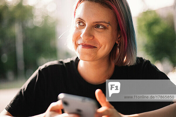 Happy young woman smiling looking away holding smart phone outdoors