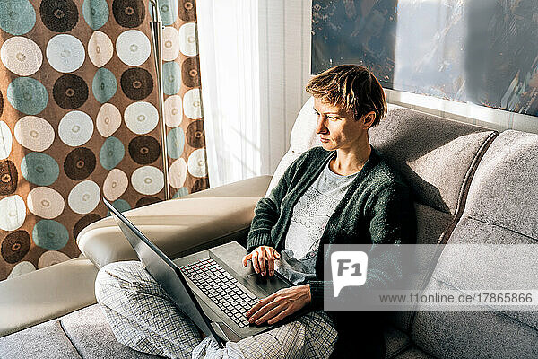Young woman works remotely sitting at home on couch in home clothes