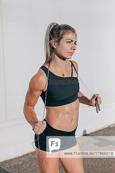 Crossfit woman standing in sunlight holding jumprope against whi