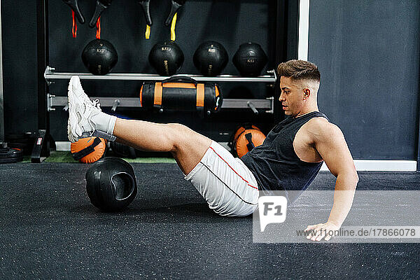 man doing strengthening exercise with ball on mat in gym