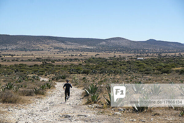 Woman running down on a trail with cactus and magueyes