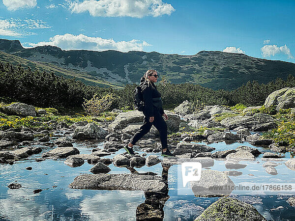 Woman walking on rocks across river in Tatras Mountains in Poland
