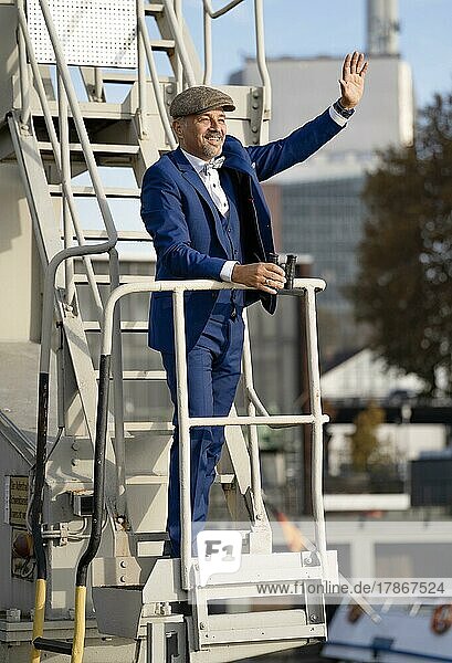 Mann mit blauen Anzug und Hut hat Fernglas in der Hand und winkt  Rheinhafen  Karlsruhe