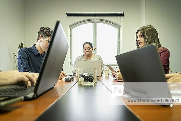 Eine Gruppe von Mitarbeitern sitzt um den Besprechungstisch im Büro und arbeitet an ihren Notebooks