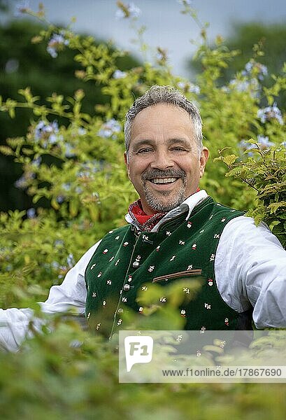 Laughing middle-aged man in Bavarian traditional costume standing by a hedge  Karlsruhe  Germany  Europe