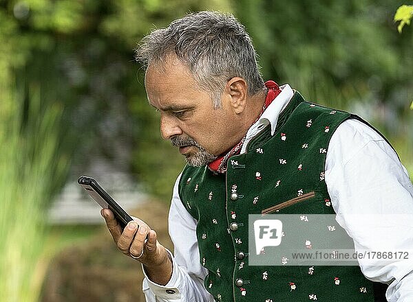 Middle-aged man in Bavarian traditional costume looking confused at his phone  Karlsruhe  Germany  Europe