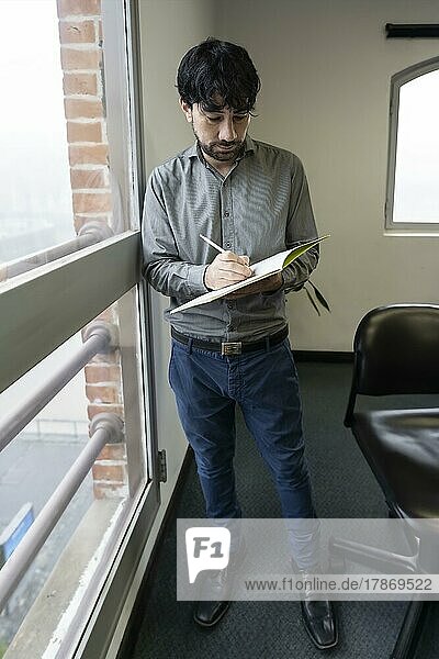 Businessman in his office  standing by the window taking notes