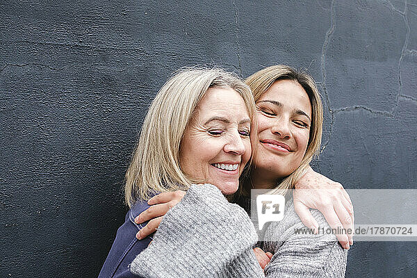 Smiling mother and daughter with eyes closed embracing each other