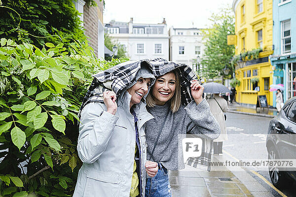 Lächelnde Mutter und Tochter unter Jacke auf dem Bürgersteig in der Stadt