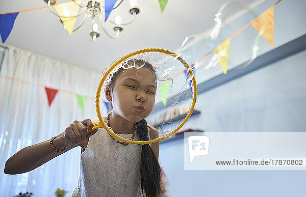 Birthday girl blowing bubbles from wand at home