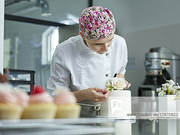 Young confectioner decorating cake with marzipan roses in kitchen