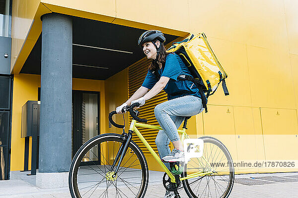 Happy delivery woman riding bicycle in front of building