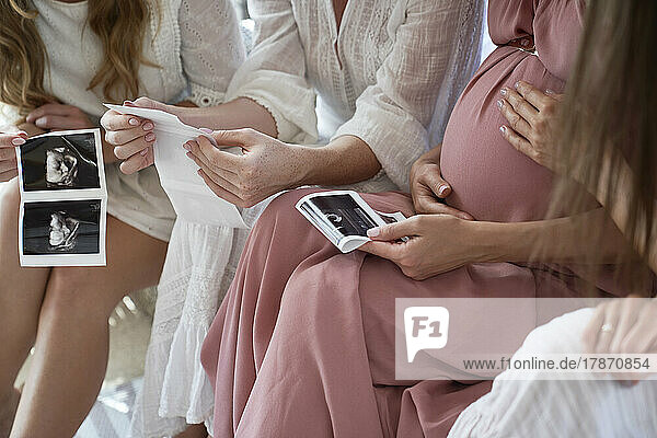 Hands of pregnant woman with friends holding ultrasound scan result at baby shower